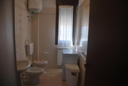 een badkamer met 2 toiletten, een wastafel en een raam bij Acquasmeralda appartamento 01 in Rosolina Mare