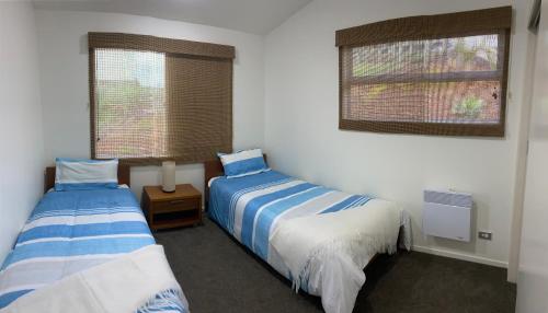 two beds in a room with two windows at Mukies Apartments in Ahipara