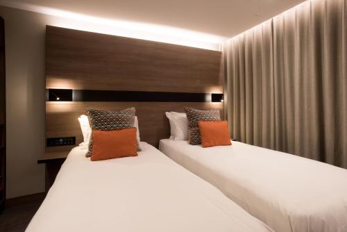 2 letti in camera d'albergo con cuscini bianchi e arancioni di Oxford Hotel a Londra
