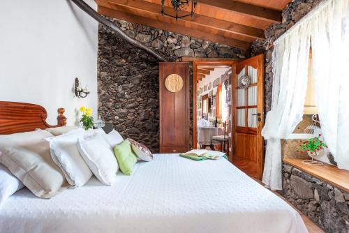 a bedroom with a white bed with a stone wall at Romantic Hamlet Cottage with Private Pool La Fragua de Eliseo in Candelaria