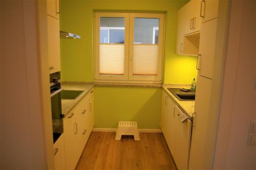 eine Küche mit grünen Wänden, weißen Schränken und einem kleinen Hocker in der Unterkunft Witt am See F in Klein Wittensee