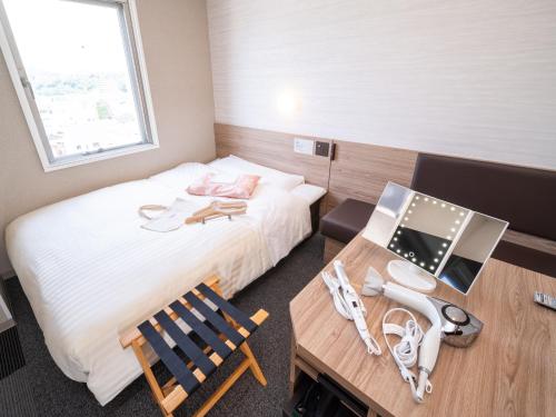a small room with a bed and a desk and a table at Super Hotel Higashi-Maizuru in Maizuru