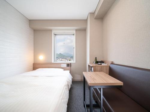 a room with a bed and a table and a window at Super Hotel Higashi-Maizuru in Maizuru