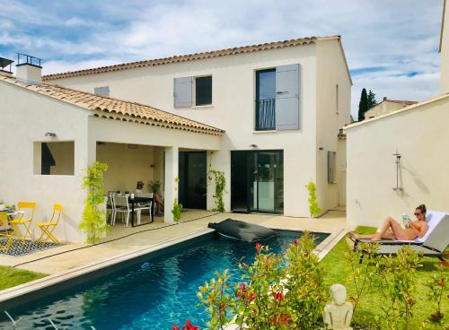 a woman sitting on a chair in front of a house with a swimming pool at La Maison d AME - for the perfect stay at the Mont Ventoux in Malaucène
