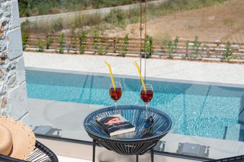 two glasses of red wine sitting on a table next to a pool at Diosas Luxury Villas in Pilaroú