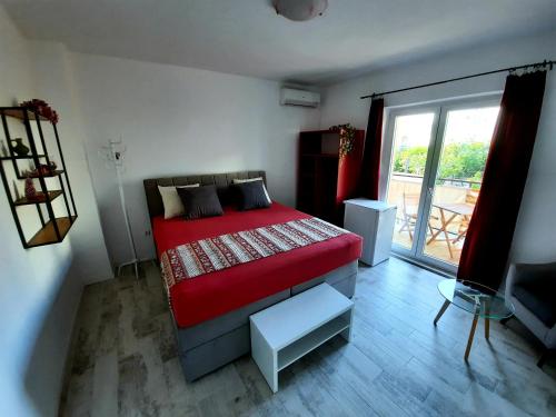 a bedroom with a red bed and a balcony at Apartments Zoro in Primošten