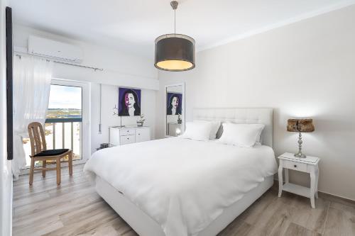 a white bedroom with a large white bed and a chair at Heritage Caeli in Portimão