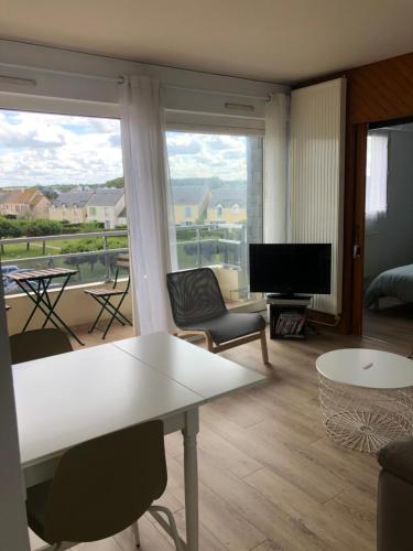 a living room with a white table and a large window at Bleu Salé - F2 Courseulles avec balcon in Courseulles-sur-Mer