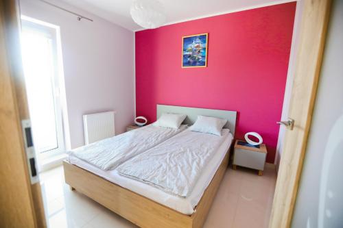 a bedroom with a bed with a pink wall at M&K Apartamenty - Marynarski in Gdańsk
