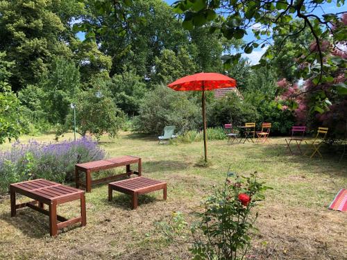 two benches and a red umbrella in a garden at La maison des amis in Nuits