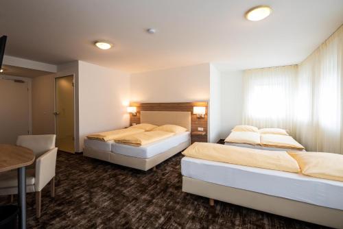 two beds in a hotel room with a table and a desk at Sternplatz Hotel in Ehingen