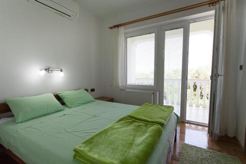 a bedroom with a bed with green sheets and a large window at Apartments Gorančica in Malinska