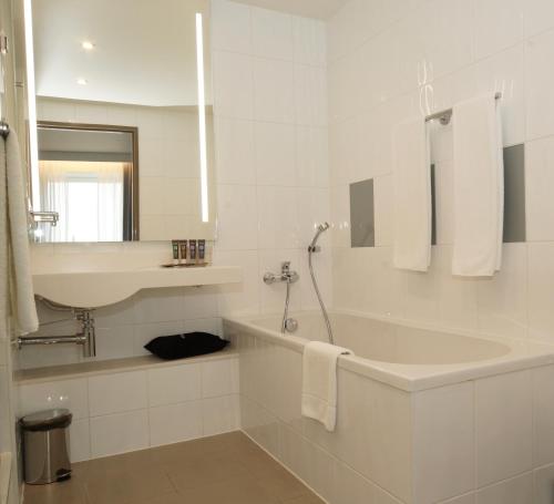 a white bathroom with a tub and a sink at Novotel Vilnius Centre in Vilnius