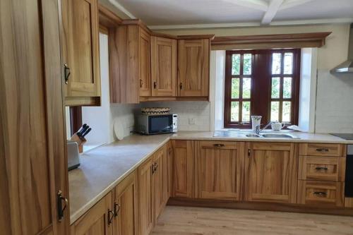 uma cozinha com armários de madeira, um lavatório e uma janela em The Gardeners Cottage at Wells House em Glenranny