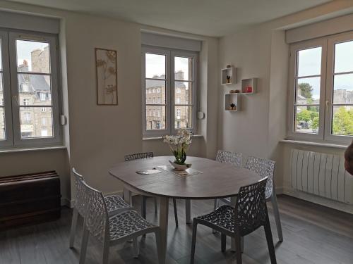 une salle à manger avec une table, des chaises et des fenêtres dans l'établissement Les appartements du Marché, à Dinan