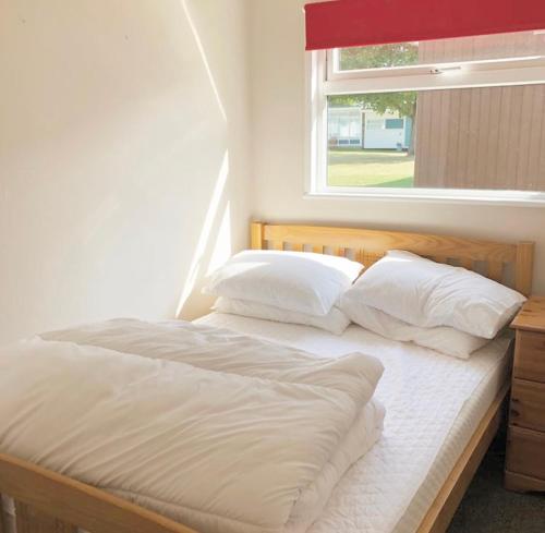 a bed with white sheets and pillows in a room with a window at Broadside Chalet Park No 90 in Norwich