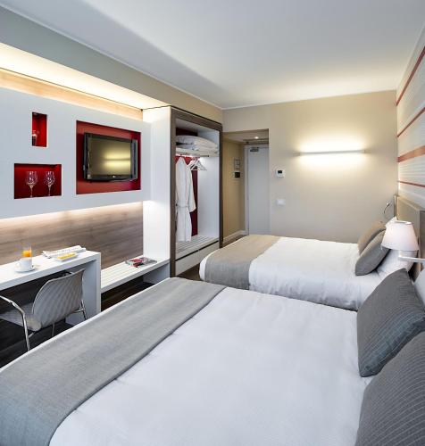 a hotel room with two beds and a desk and a tv at Enjoy Garda Hotel in Peschiera del Garda