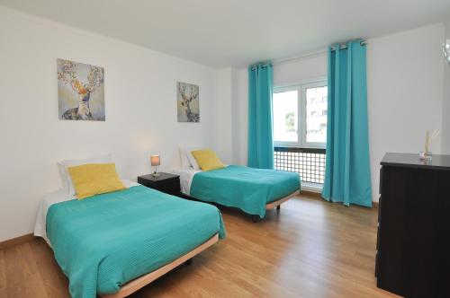 a bedroom with two beds and a window with blue curtains at Tenis Golf Mar by OCvillas in Quarteira