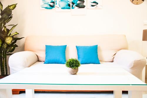 eine weiße Couch mit blauen Kissen und eine Pflanze darauf in der Unterkunft AlohaMundi Zaragoza III in Sevilla