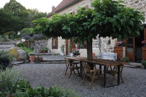 einen Holztisch und Stühle unter einem Baum im Garten in der Unterkunft La Belle Âme in Saint-Priest-des-Champs