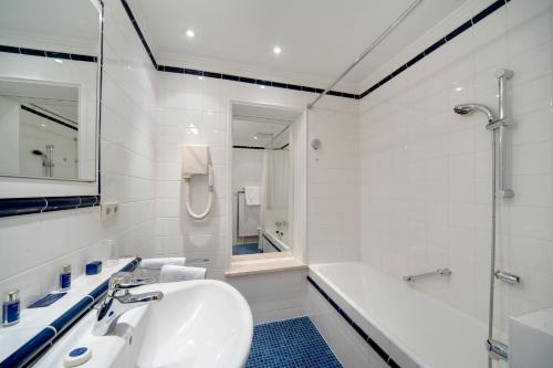 La salle de bains est pourvue d'un lavabo, d'une baignoire et d'une douche. dans l'établissement Grand Hotel Cravat, à Luxembourg