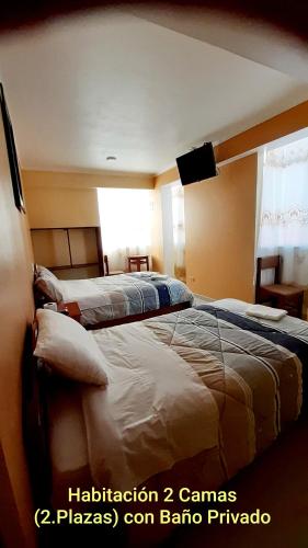 a bedroom with two beds and a tv on the wall at Hostal Capac in Ayacucho