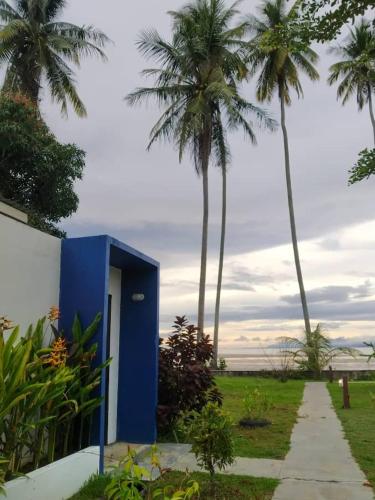 a blue building next to palm trees and a sidewalk at Rafflesia Resort in Lundu