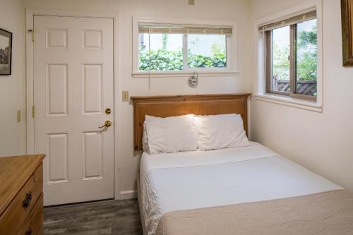 a bedroom with a bed and two windows at Andril Fireplace Cottages in Pacific Grove