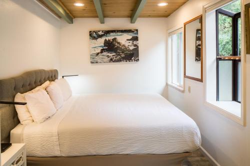 a bedroom with a white bed and two windows at Andril Fireplace Cottages in Pacific Grove
