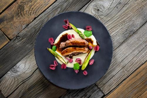 a black plate with meat and vegetables on a wooden table at Hotel Wisła Premium in Wisła