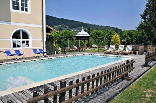 a swimming pool with blue chairs and a house at Alpen Hotel Eghel in Folgaria