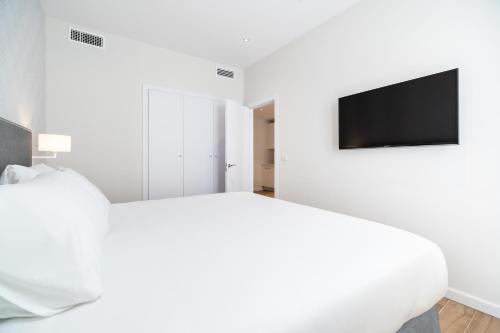 a white bedroom with a bed and a flat screen tv at Tandem Puerto Chico in Cádiz
