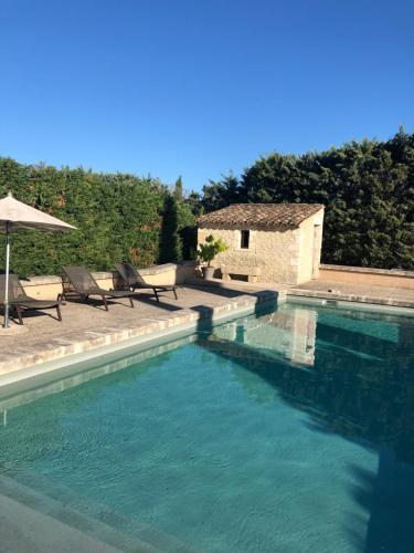 une piscine avec deux chaises et un parasol dans l'établissement Gîte Les Alpilles, à Eygalières