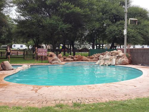 a swimming pool in a park with a rock waterfall at Sondela Nature Reserve & Spa Moselesele Tents in Bela-Bela