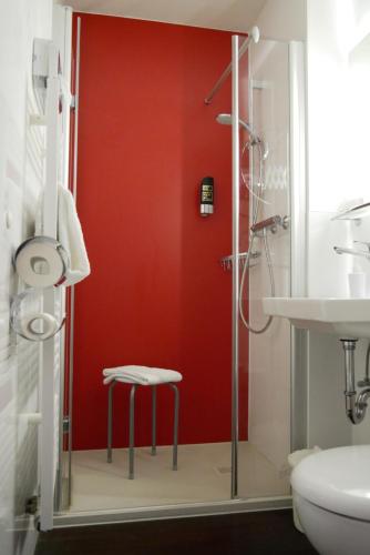 La salle de bains est pourvue d'un mur rouge et d'un tabouret à côté d'une douche. dans l'établissement Wohlfühlhotel Saxonia, à Bad Kissingen