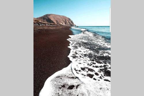 a beach with black sand and water and a mountain at Etoile apartment in Perissa
