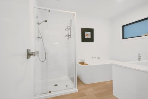 a white bathroom with a shower and a tub at Sky Above Beach Below - Waihi Beach Holiday Home in Waihi Beach