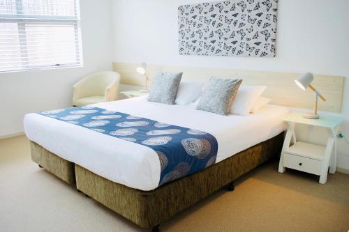 a white bed with a white comforter and pillows at The Coast Motel in Yeppoon