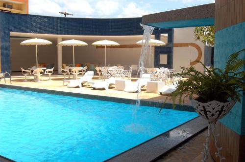 una piscina con sillas, sombrillas y una fuente en Hotel Praia Ponta d'Areia, en São Luís