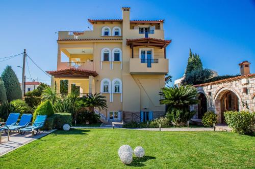 a large yellow house with a yard with chairs at Lagonisi Villa VIP in Lagonissi