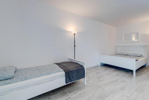 a white bedroom with two beds and a lamp at Pod Winogronem - Apartamenty z basenem i wyżywieniem in Pobierowo