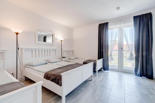 a white bedroom with two beds and a window at Pod Winogronem - Apartamenty z basenem i wyżywieniem in Pobierowo