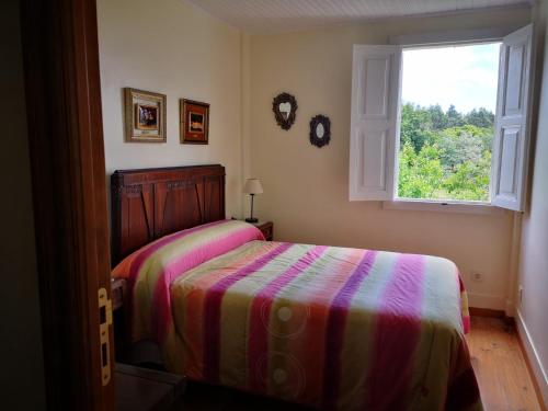 een slaapkamer met een bed met een gestreepte deken en een raam bij Casa "A Rúa" - Preciosa casa en la montaña con amplio jardín in Vilariño