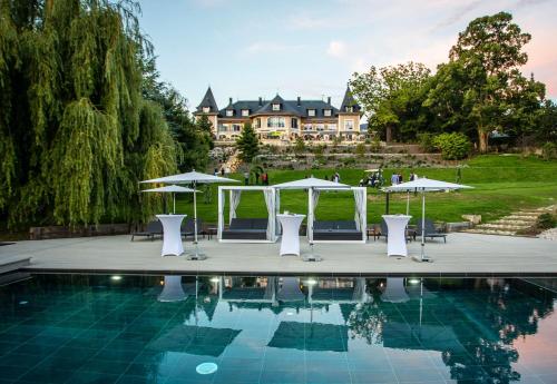 a pool with tables and umbrellas in front of a mansion at Hôtel L'Incomparable Aix-Les-Bains in Tresserves