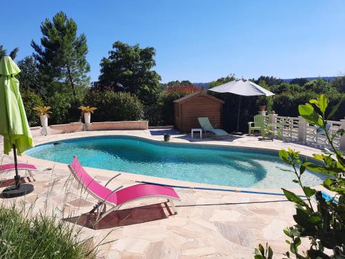 a swimming pool with pink chairs and an umbrella at Villa Lei Rigaü in Salernes