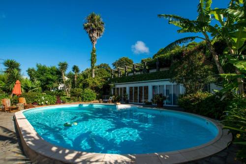 a swimming pool in front of a house with a palm tree at Quinta Minuvida in Rabo de Peixe