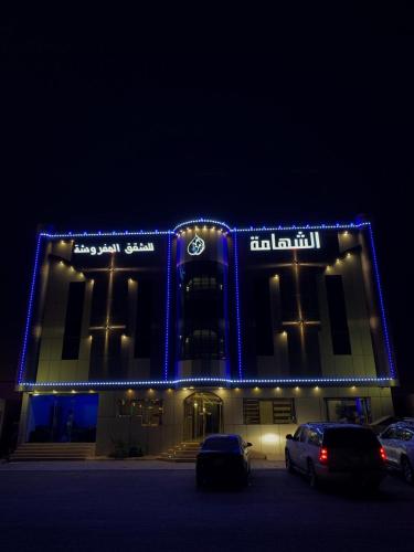 um edifício iluminado com carros estacionados num parque de estacionamento em Alshahamah Hotel Apartments em Najran