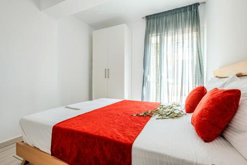 a bedroom with a bed with red pillows and a window at Design Suites Efharis (Sauvignon) in Nea Peramos