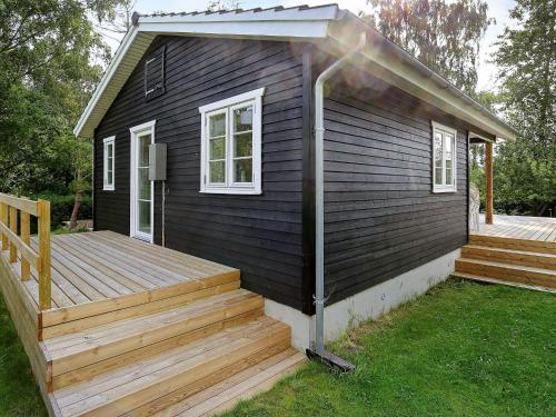 ein kleines schwarzes Haus mit einer Holzterrasse in der Unterkunft 4 person holiday home in Skibby in Skibby