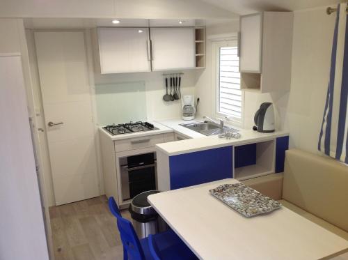 une cuisine avec des armoires blanches et bleues et une table dans l'établissement TopSun Argelès Camping La Sirène 2 bedroom 25m2 max 4 personnes Inc bebe pas d'enfants sans parents, à Argelès-sur-Mer